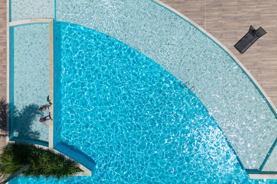 Two kids relax at the edge of clear blue pool during sunny summer vacation. This aerial view captures family,  friends, fun, and recreation at resort, relaxation and joyful outdoor moments.