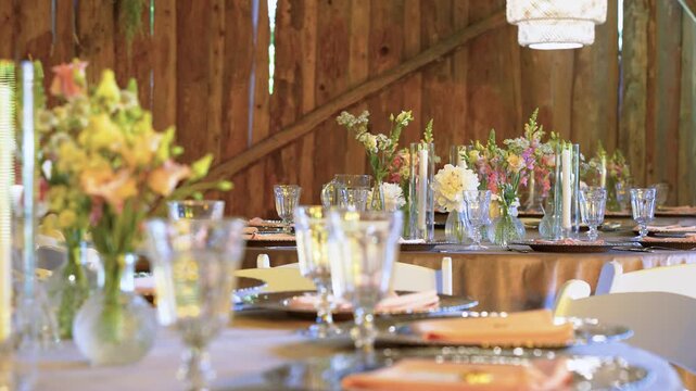 Charming rustic barn wedding reception setup featuring tables with elegant glassware, fresh floral centerpieces, soft golden lighting, and wooden walls for a cozy, romantic atmosphere.