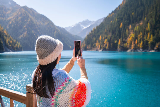 Young female tourist enjoying and taking a photo at beautiful autumn scenery landscape at jiuzhaigou national park in Sichuan, China