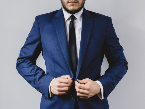 Professional man adjusting his navy blue suit jacket with white shirt and black tie against plain background