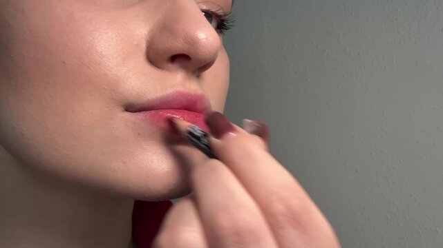 Woman applying lip liner, using a cosmetic pencil to define mouth shape, outlining lips with precision, performing a daily beauty routine for facial enhancement.