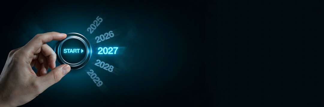 Hand turns a rotary dial to select the year 2027 with start button illuminated in blue light future ahead new beginnings technology concept representing transition.