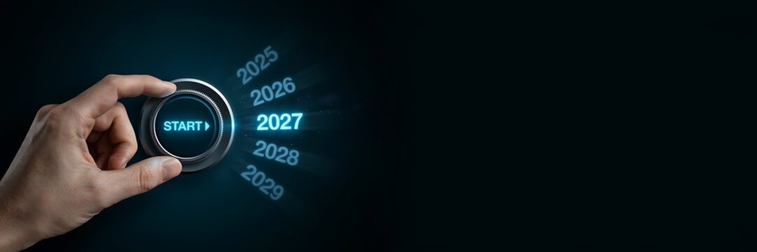 Hand turns a rotary dial to select the year 2027 with start button illuminated in blue light future ahead new beginnings technology concept representing transition.