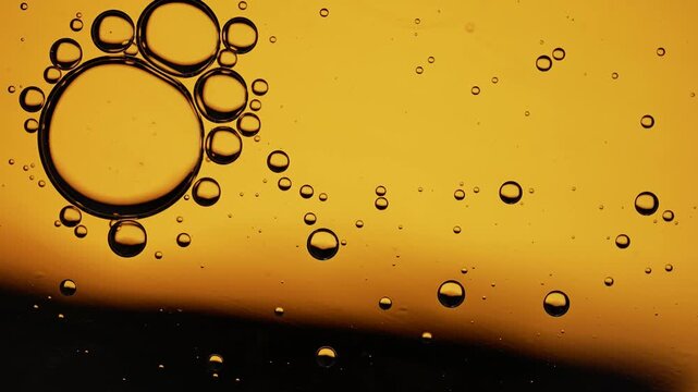 Macro oil droplets rising and merging against warm orange background