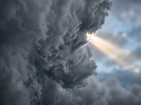 Dramatic sunbeam breaking through dark storm clouds in a moody overcast sky.