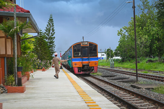 Traditional thai train is pulling into rural station with person standing and waving green flag to signal safety. authentic atmosphere of northern thailand rail travel