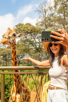 Close up Cheerful female tourist blogger take selfie feeds tall Rothschild giraffe from elevated observation platform, Giraffe Centre Langata Nairobi Kenya eco travel wildlife conservation lifestyle