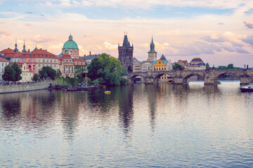 Fototapeta premium The historic Charles Bridge in Prague and the city's charming architecture across the calm surface of the Vltava River during sunset.
