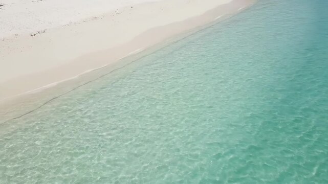 Aerial view straight down of calm beach with shallow gradient water and soft daylight in summer