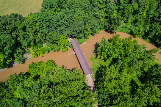 Covered bridge spanning muddy river surrounded by green forest