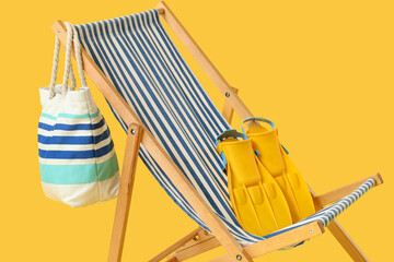 Beach chair with striped bag and yellow flippers on yellow background © Pixel-Shot