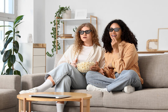 Two young women watching 3d movie at home with popcorn
