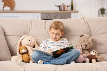 Obraz premium Cute little boy with knitted toys reading story on sofa at home
