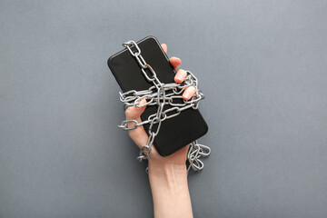 Naklejka premium Female hand with modern mobile phone and chain on grey background, closeup