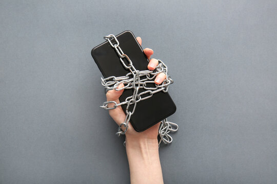 Female hand with modern mobile phone and chain on grey background, closeup