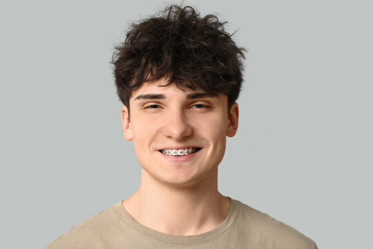 Smiling young man with dental braces on light background
