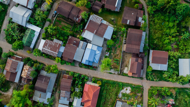 Aerial View of a serene rural village with green garden in Northeast Thailand. Tranquil landscape and authentic cultural heritage. Rural community in Thailand with old galvanized roof. Rural building.