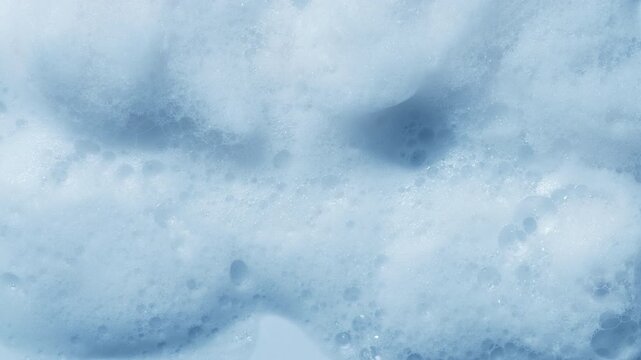 Overhead capture of a pale blue soap sud surface with mounds and dips orbiting light casts dynamic shadows