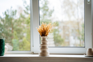 A vase of abstract shape stands in the middle of a light window sill in the workshop. Bouquet of yellow dried flowers in a vase. © Nimesh
