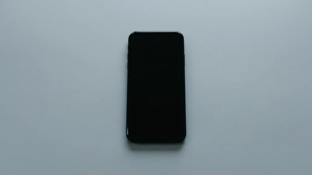Black smartphone with blank screen on plain surface