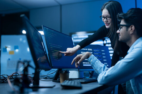Asian happy woman and man programmer team coding software at computer in dark tech office, Concept of digital transformation, modern cyber security, startup teamwork and future IT digital network