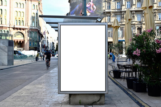 bus shelter at busstop. white poster ad display space and lightbox. mockup template. blank ad panel. glass design. urban street setting. soft background. silhouettes in a distance