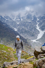 Naklejka premium Hiker trekking on a rocky mountain trail at Kareri Lake in Dharamshala with snowy peaks in background