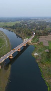 Aerial drone view of a long concrete bridge spanning a wide dark river connecting rural