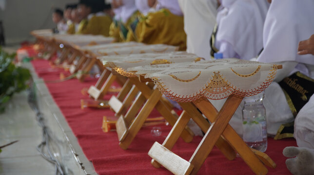 Row of small wooden folding desks or rehal on a red carpet at an Islamic school event. Concept of Quran education, Muslim student graduation, madrasah ceremony, and religious learning.