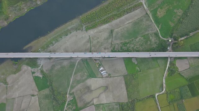 Aerial drone view of a long elevated highway bridge crossing a river and agricultural fields with