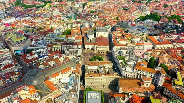 Milan, Italy. Drone footage over the historic center revealing the glass dome of Galleria Vittorio Emanuele II, Teatro alla Scala, and the Gothic spires of Duomo di Milano under an overcast sky.. Dro