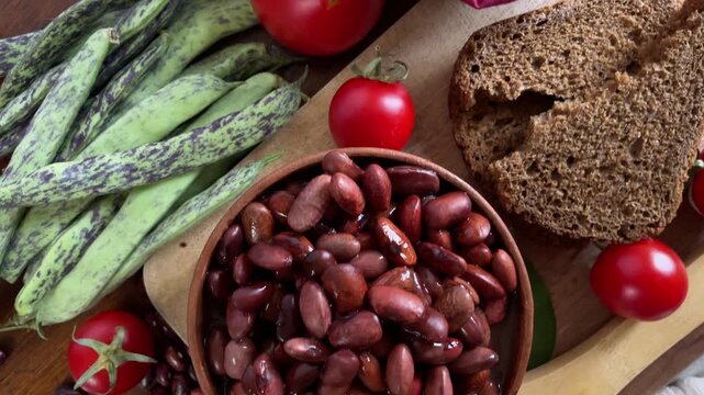 Smooth camera movement over cooked and raw kidney beans, fresh tomatoes, garlic, and rye bread on a rustic table