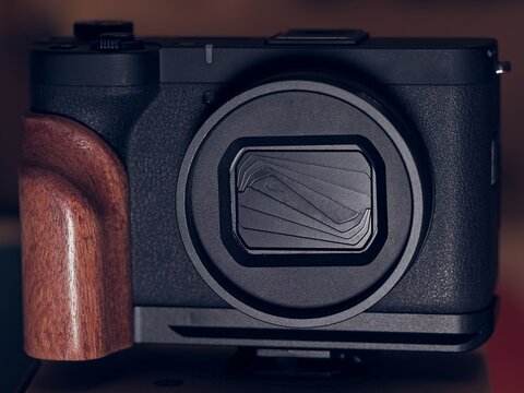 Close up shot of a sleek black digital camera body featuring an integrated lens barrier and a custom ergonomic brown wooden handgrip