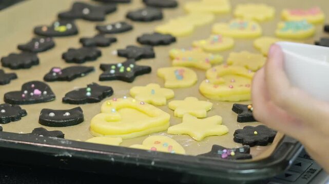 Close-up of a young girl's hands carefully decorating shaped cookie dough with colorful drag&eacute;es and sprinkles on a baking tray. A fun domestic lifestyle scene of an elementary school child making home