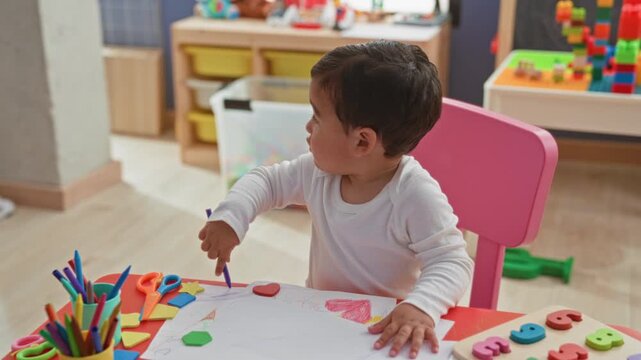 Boy drawing with a purple crayon, hand pointing at paper on a pink chair in a building; curiosity learning.