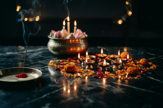 Traditional Diwali diya lamps with burning incense and marigold flowers, spiritual Hindu puja ceremony setup on dark marble, glowing oil lamps and lotus petals