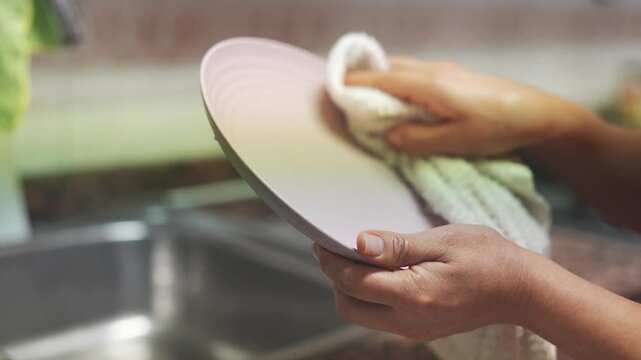 Female hands carefully drying a freshly washed plate with a cloth over the kitchen sink