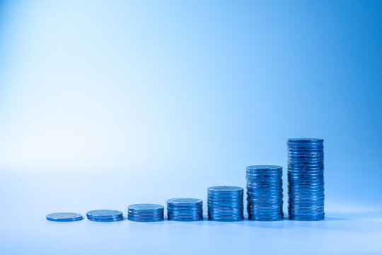 Stacked coins arranged in ascending order on a blue background, symbolizing financial growth, wealth accumulation, investment, savings, business success, and economic development. Minimal composition 