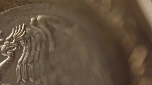Macro view of eagle and snake engraving on coin surface, highlighting raised relief details, metallic texture, and symbolic design elements in close perspective.
