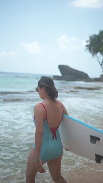 Asian Woman in Her 30s Carrying a Blue Surfboard on a Sri Lankan Beach