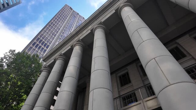 Striking low-angle footage of the Old Federal Reserve Bank Building in San Francisco, featuring imposing neoclassical columns, urban skyscrapers, and lush trees under bright natural daylight.