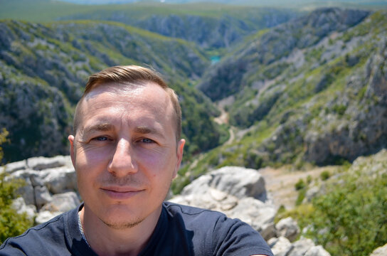 A male traveler poses against the spectacular Zrmanja Canyon in Croatia, surrounded by rugged cliffs and Mediterranean wilderness. The authentic travel portrait conveys exploration and adventure.