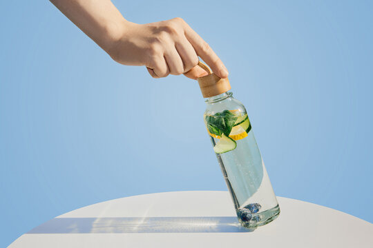 Hand holding glass bottle with refreshing fruit and herb infused detox water