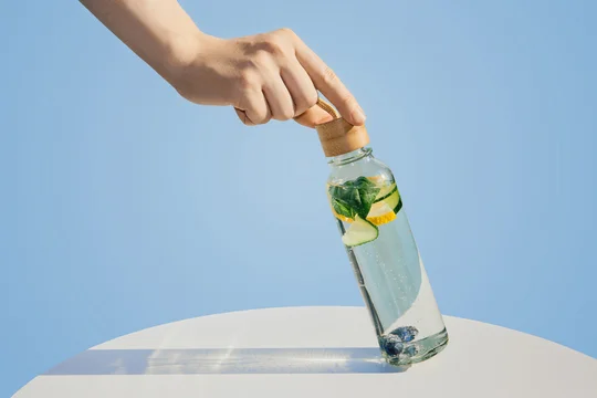 Hand holding glass bottle with refreshing fruit and herb infused detox water