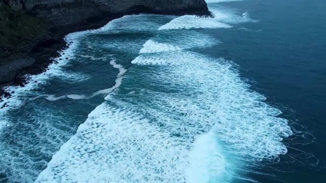 Aerial drone view of massive ocean surf patterns crashing against a rocky coastline in cinematic style