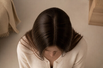 Fototapeta premium A person with long dark hair wearing a cream-colored sweater is shown in a softly lit indoor setting.