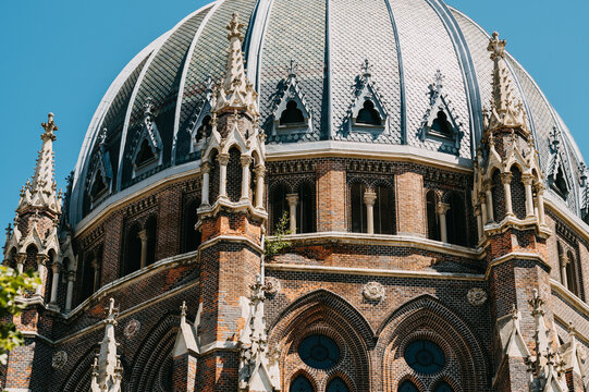 Low angle shows brick cathedral dome, ornate spires, arched windows and textured roof tiles in bright sun