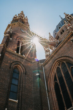 Sunlight flares between tall brick towers of historic cathedral viewed from ground level against blue sky