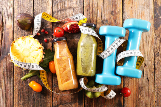 Healthy fruit smoothies in glass bottles with dumbbells and measuring tape on wood. Diet or healthy eating concept