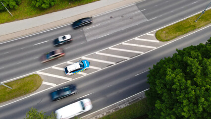 Overhead view of an Estonian police vehicle positioned at the roadside, observing traffic flow and monitoring speed limits, with several cars moving past with motion blur on a summer day © Dark Artistic